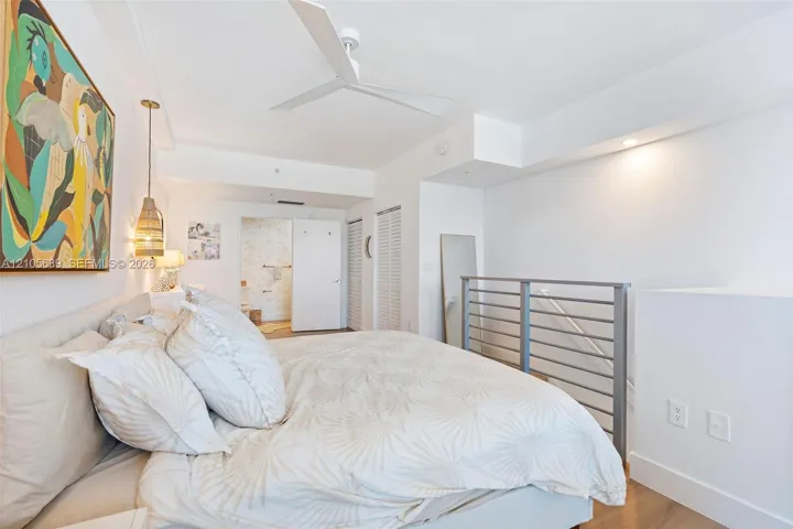 White-painted interior featuring a three-blade ceiling fan, metal horizontal-bar railing, louvered-style closet doors, and wood-finish flooring
