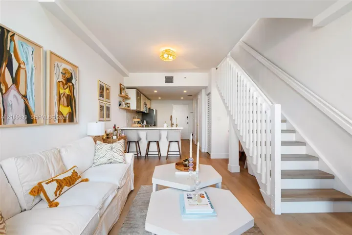Open-concept interior featuring wood-finish flooring, a white staircase with vertical balusters, a peninsula with stone-finish countertops, and flush-mount lighting