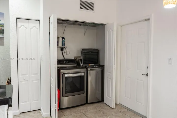 Laundry closet featuring bi-fold doors, tiled flooring, and stacked appliances
