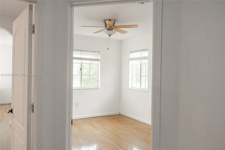 Wood-finish flooring with a ceiling fan light fixture and two windows with blinds