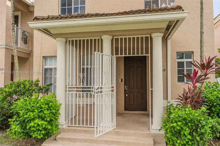Covered entry with prominent columns, a paneled entry door, and decorative ironwork