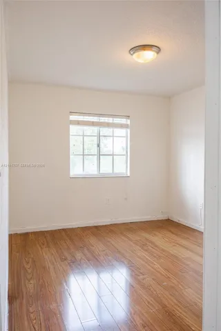 Wood-finish flooring with a window featuring horizontal blinds and a flush mount ceiling light