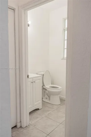 White vanity with dual cabinet doors, light-toned tile flooring, and a window