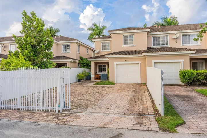 Two-story stucco exterior with white grid windows, barrel tile roof, and a private entry gate