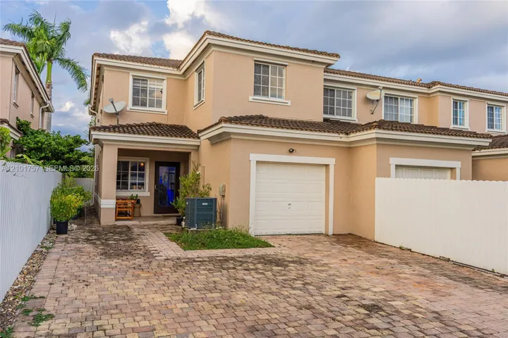 Stucco exterior with a terracotta tile roof, paver driveway, and an attached garage