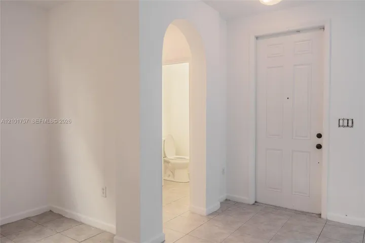 White paneled door, arched doorway, and light-toned tile flooring