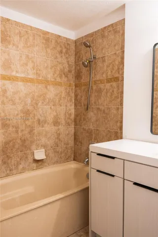 Bathtub with full-height tile surround, wall-mounted shower fixture, and a vanity with a light-toned countertop