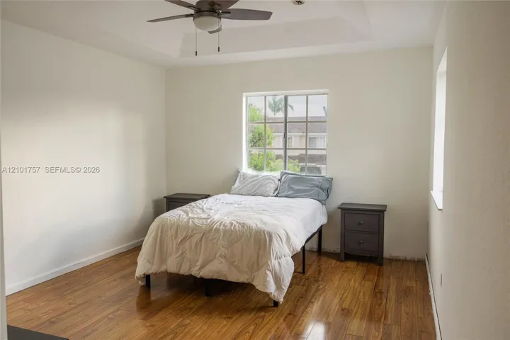 Tray ceiling with a ceiling fan, wood-finish flooring, and a large window