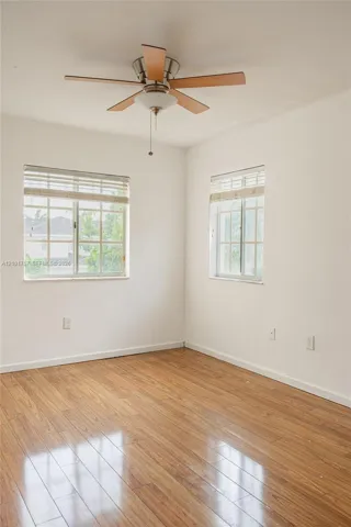 Wood-finish flooring throughout, two windows with blinds, and a ceiling fan with integrated lighting