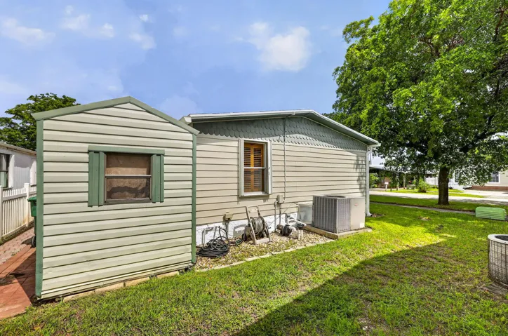 Exterior featuring horizontal siding, green trim accents, an outdoor storage shed, and a mature shade tree