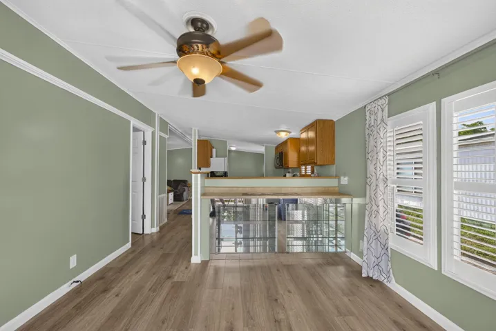 Wood-finish flooring throughout, ceiling fan with integrated lighting, wood wall paneling, and two windows with white plantation shutters
