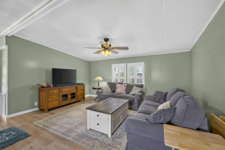 Spacious living area featuring light green walls, wood-finish flooring, a ceiling fan with integrated lighting, and plantation shutters