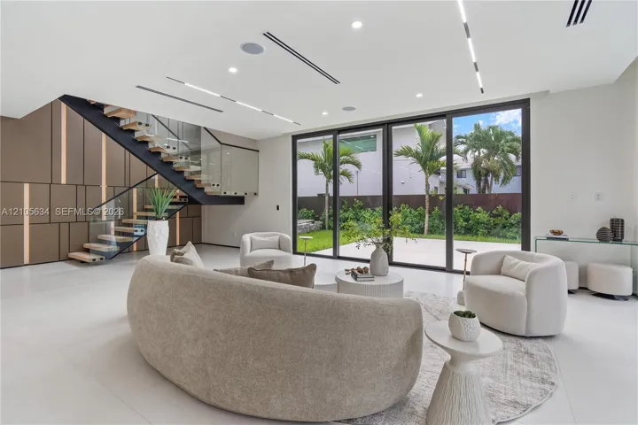 Open-concept interior featuring large-format tile flooring, a custom metal staircase with a glass railing, built-in decorative wall paneling, and floor-to-ceiling sliding glass doors