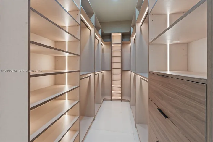 Walk-in wardrobe featuring custom cabinetry with wood-finish drawer fronts, open shelving, integrated vertical LED lighting, and matte black hardware