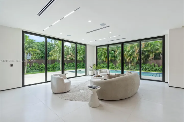 Large-format sliding glass doors, polished porcelain flooring, recessed linear lighting, built-in ceiling speakers, and perimeter patio access