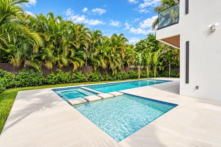 In-ground swimming pool with an integrated spa, featuring stone-style paver decking, decorative concrete stepping stones, and surrounding lush landscaping
