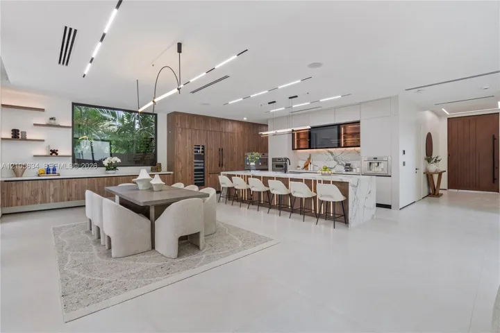 Open-concept kitchen featuring a waterfall-edge stone island, built-in panel-ready appliances, wood-finish cabinetry, linear recessed ceiling lighting, and porcelain tile flooring