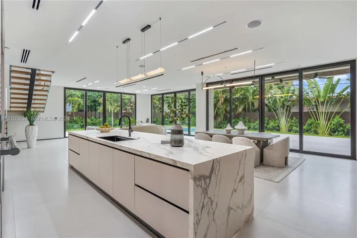 Kitchen featuring a large central island with waterfall-edge stone countertops, custom flat-panel cabinetry, matte black hardware, floor-to-ceiling multi-panel sliding glass doors, and recessed linear LED ceiling lighting