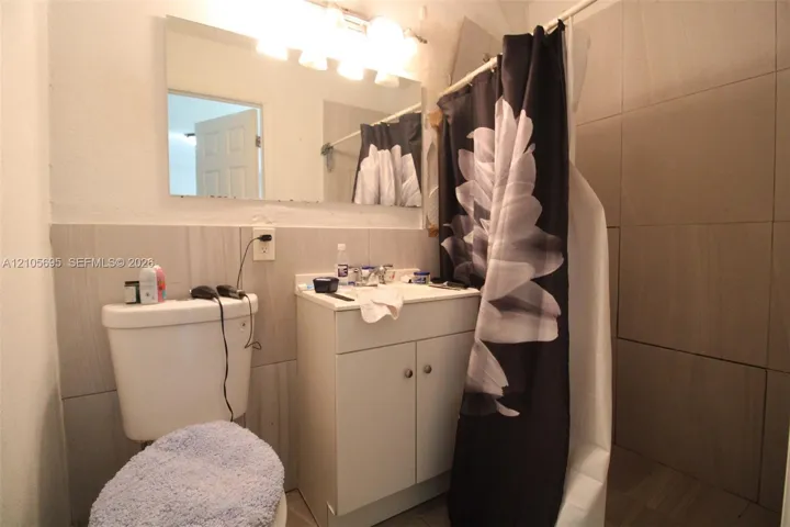 Bathroom featuring large-format neutral wall tiling, a vanity cabinet with a sink, a wall-mounted vanity mirror, and a multi-bulb light fixture