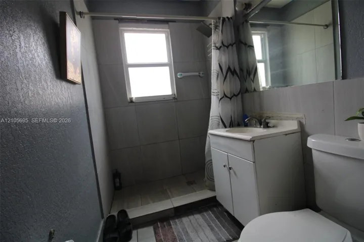 Bathroom featuring a tiled shower enclosure, white vanity cabinet with a integrated sink, wall-mounted mirror, and tile flooring