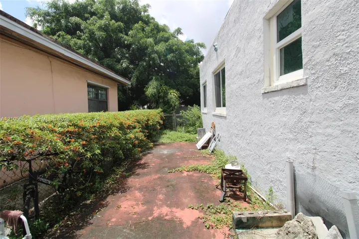 Exterior side yard featuring stucco wall cladding, sliding windows, and a paved walkway bordered by mature hedge shrubbery
