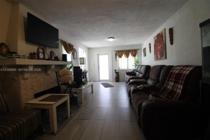 Living area featuring large-format tile flooring, a textured fireplace mantle with a stone-finish surround, and a glass-paned exterior entry door
