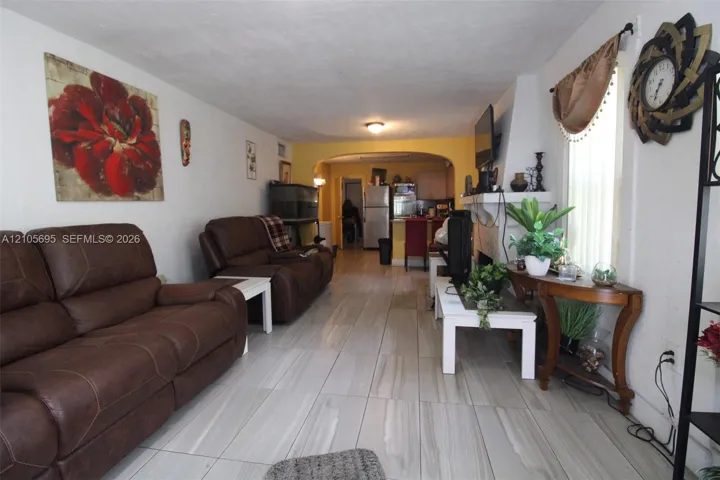 Large-format tile flooring, masonry fireplace with a white mantel, and an arched entryway