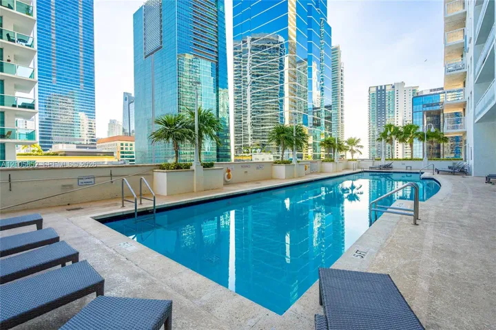 Outdoor swimming pool featuring a tiled deck, metal handrails, integrated planter boxes, and palm tree landscaping