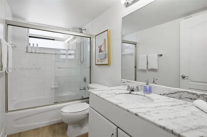 Bathroom featuring a vanity with a natural stone countertop, undermount sink, full-width vanity mirror, and a shower-tub combination with a sliding glass door and tiled surround