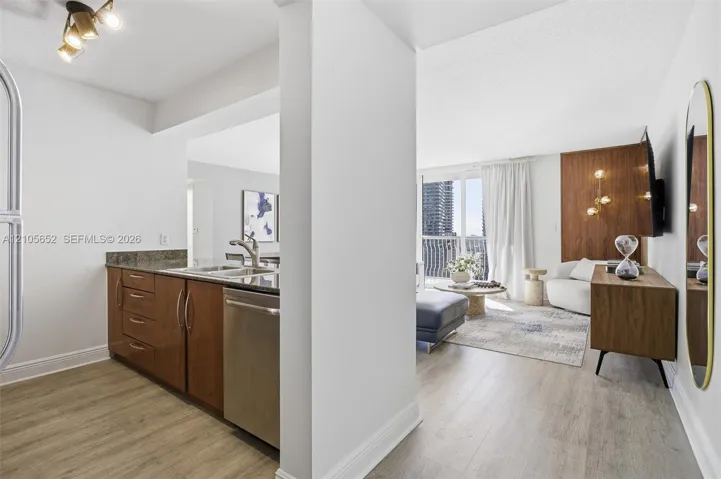 Kitchen featuring dark wood-finish cabinetry, stone countertops, and stainless steel dishwasher, complemented by wood-finish flooring and a decorative wood-paneled accent wall