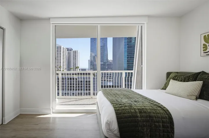 Floor-to-ceiling sliding glass door, private balcony with metal railing, and neutral wood-finish flooring