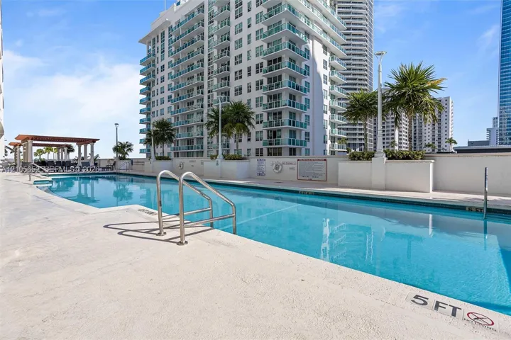 Swimming pool with concrete decking, metal handrails, and a wooden pergola structure