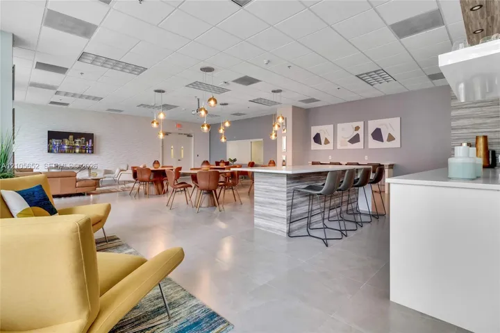 Large common area featuring tile flooring, a stone-finish kitchen island with seating, drop pendant lighting, and textured wall accents