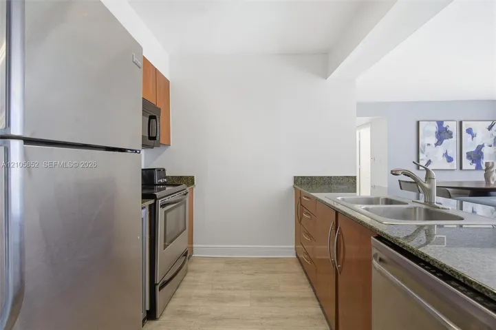 Kitchen featuring stainless steel appliances, stone countertops, wood-finish cabinetry, and a double-basin undermount sink