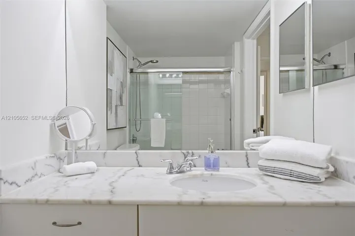 Bathroom featuring a stone vanity top with an integrated oval sink, polished chrome faucet, full-width mirror, and a walk-in shower with tiled surround and sliding glass doors