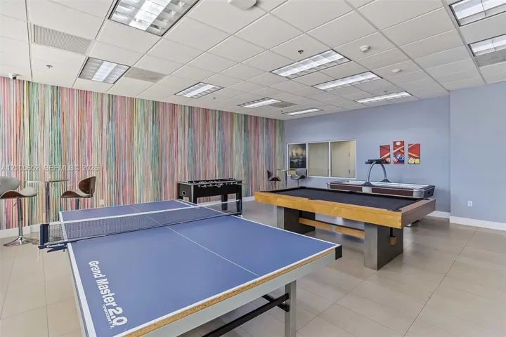Spacious recreational area featuring a drop ceiling with integrated lighting, tile flooring, and a decorative multi-color vertical-stripe accent wall