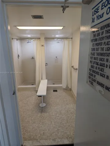 Dual shower stalls featuring tile surround, mosaic floor tiling, wall-mounted metal grab bars, and recessed lighting