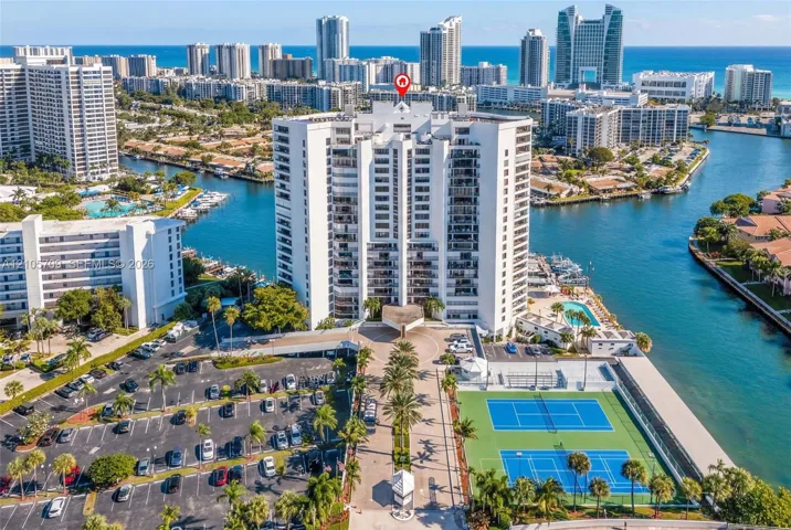 High-rise residential building featuring private balconies, dual tennis courts, an outdoor swimming pool, and dedicated parking