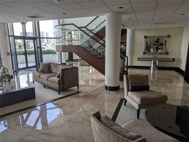 Polished stone flooring, floor-to-ceiling glass paneling, and an open staircase featuring metal railing with geometric detailing