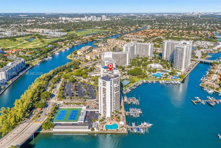 Aerial view of high-rise building featuring a swimming pool, two tennis courts, and on-site boat slips located on the waterfront