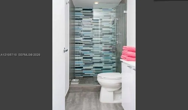 Walk-in shower with multi-colored glass tile accent wall, frameless glass enclosure, handheld shower fixture, and wood-finish flooring