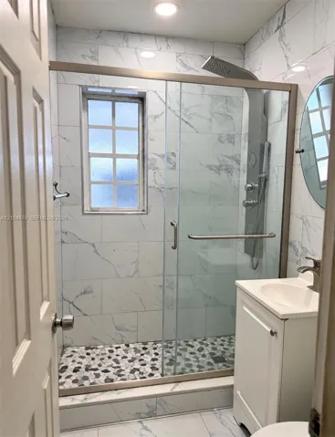 Glass-enclosed shower with pebble-finish flooring, white tile surrounds, and a multi-function shower system