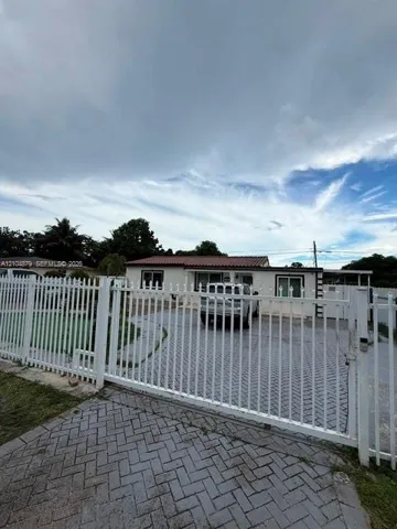 White metal security gate, paver driveway, and a single-story residence with a red tile roof