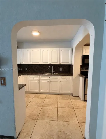 Kitchen featuring white cabinetry, dark stone countertops, stainless steel sink with a gooseneck faucet, and tile flooring