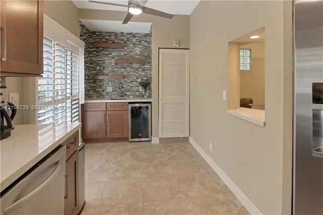 Wet bar featuring custom wood cabinetry, stone-tiled backsplash, built-in beverage refrigerator, floating wood shelving, and stone tile flooring