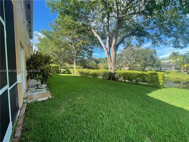 Expansive lawn area with mature shade trees, stone ground cover accents, and natural water frontage