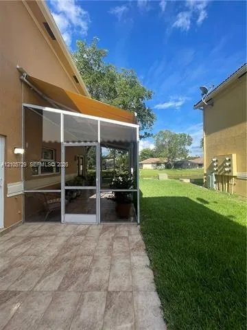 Screened-in patio with tiled flooring and retractable awning, featuring an open-air concrete patio and expansive grass lawn