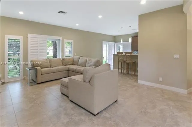 Open-concept interior featuring large-format tile flooring, recessed lighting, white louvered plantation shutters, and a kitchen breakfast bar with pendant lighting