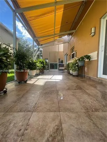 Covered screened-in lanai featuring large-format ceramic tile flooring, a retractable fabric awning, and a wall-mounted exterior light fixture