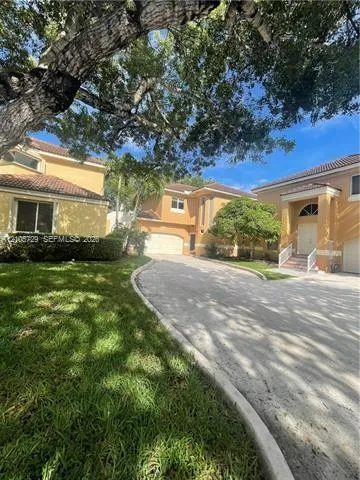 Stucco exterior featuring tile roofing, multi-car garages, and an expansive paved driveway lined with mature landscaping
